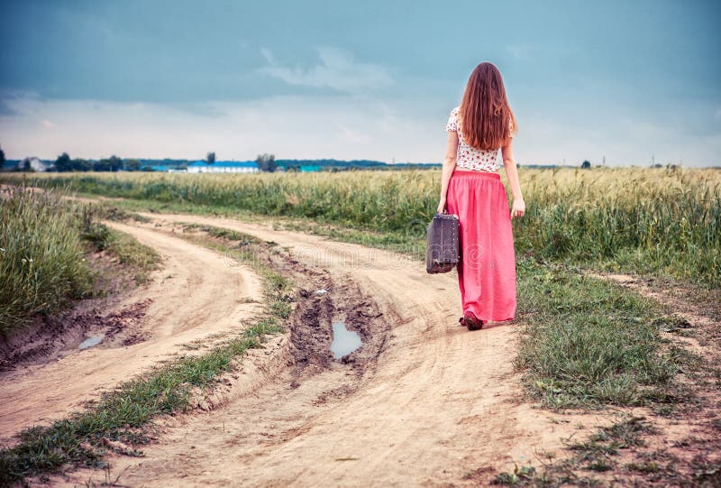 Walking girl with old suitcase on the road