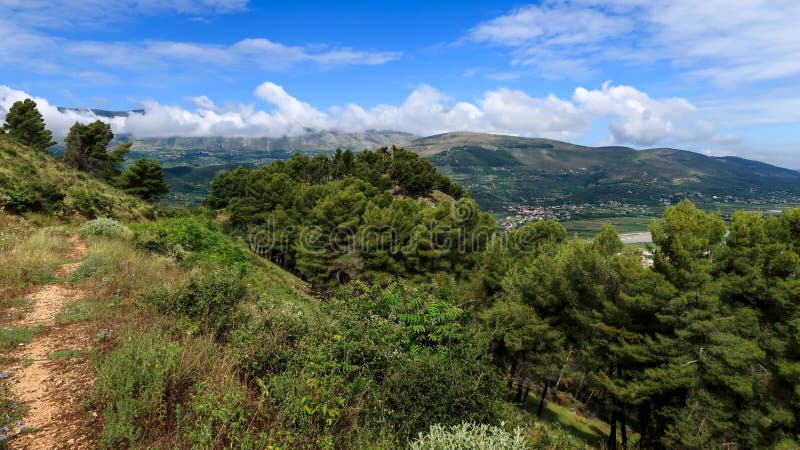 Walking path in lovely green nature with clouds and mountains in the background during a sunny day, Berat