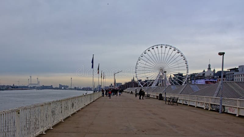 Walkway along river Scheldt with ferris wheel in the city of Antwerp. Walkway along river Scheldt with ferris wheel and wind turbines in the distance in the city royalty free stock images Walkway along river Scheldt with ferris wheel in the city of Antwerp. Walkway along river Scheldt with ferris wheel and wind turbines in the distance in the city royalty free stock images