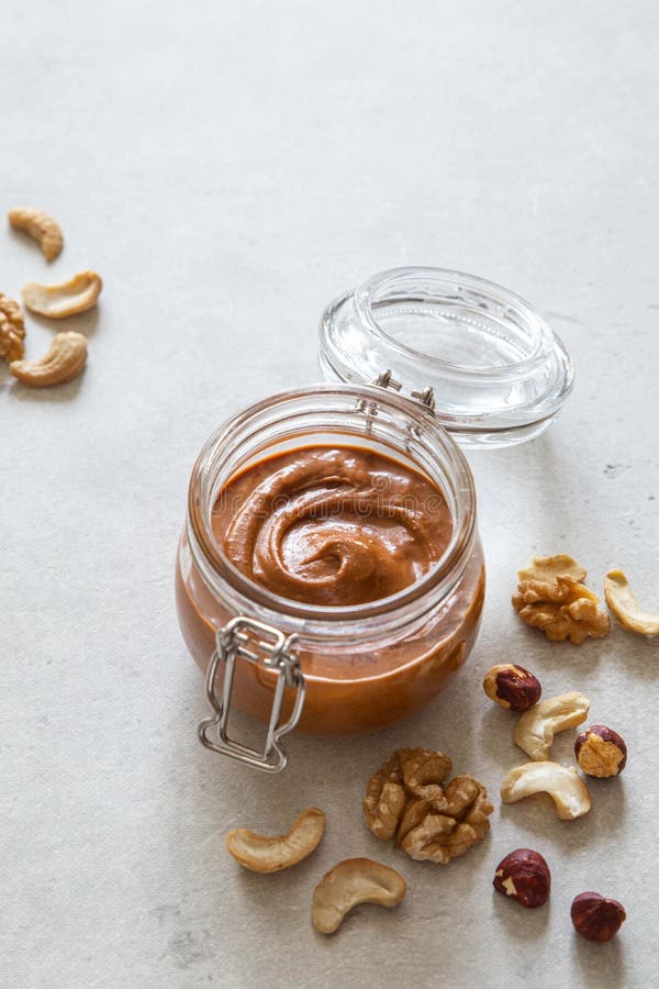 Walnut, hazelnut and cashew nut butter in glass jar on light background. Homemade raw organic mixed nuts spread.