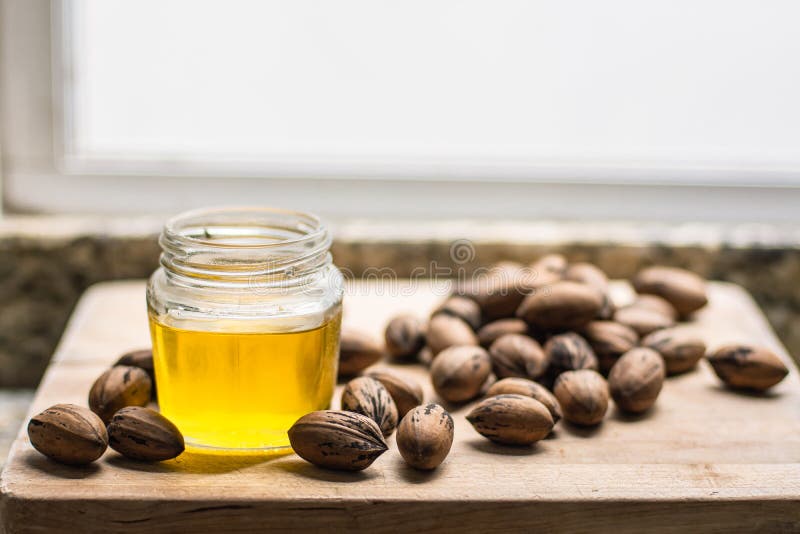 Natural Walnut oil in a jar next to some delicious nuts are on a wooden table. Natural Walnut oil in a jar next to some delicious nuts are on a wooden table