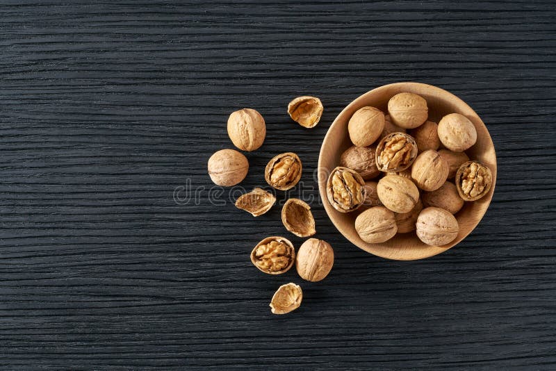 Walnuts in Wooden Bowl on Black Table with Copy Space. Top View Stock