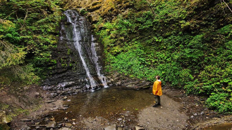 Wanderer Mann in gelben Regenmantel genießen die Aussicht auf Wasserfall im Wald