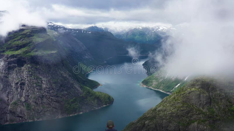 Wanderer mit Blick auf den norwegischen Fjord und die Berge an einem bewölkten Tag