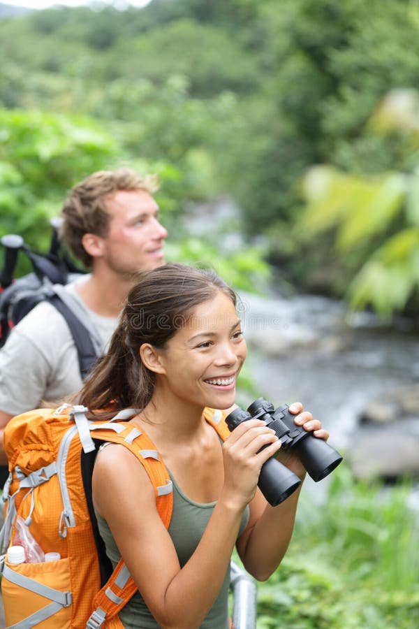 Hiking couple of hikers in outdoor activity wearing backpacks. Woman hiker looking with binoculars smiling happy. Healthy lifestyle image from Iao Valley State Park, Wailuku, Maui, Hawaii, USA. Hiking couple of hikers in outdoor activity wearing backpacks. Woman hiker looking with binoculars smiling happy. Healthy lifestyle image from Iao Valley State Park, Wailuku, Maui, Hawaii, USA.