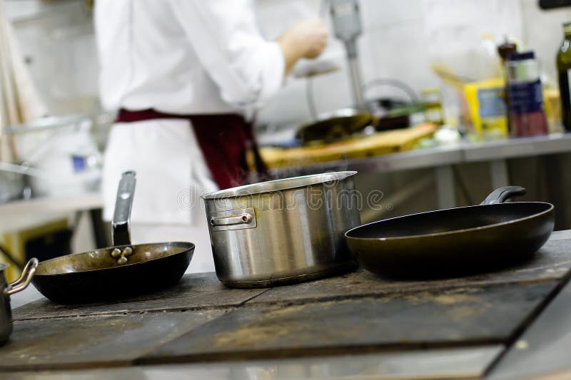 Pans on the stove in a professional kitchen with the cook on a background. Pans on the stove in a professional kitchen with the cook on a background