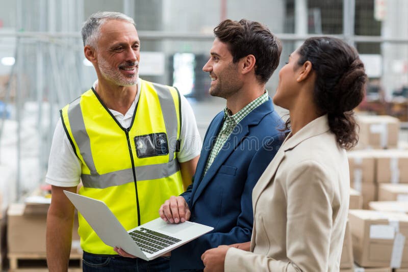 Warehouse managers and worker discussing with laptop stock image