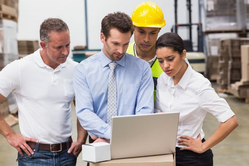 Warehouse managers and worker looking at laptop stock images