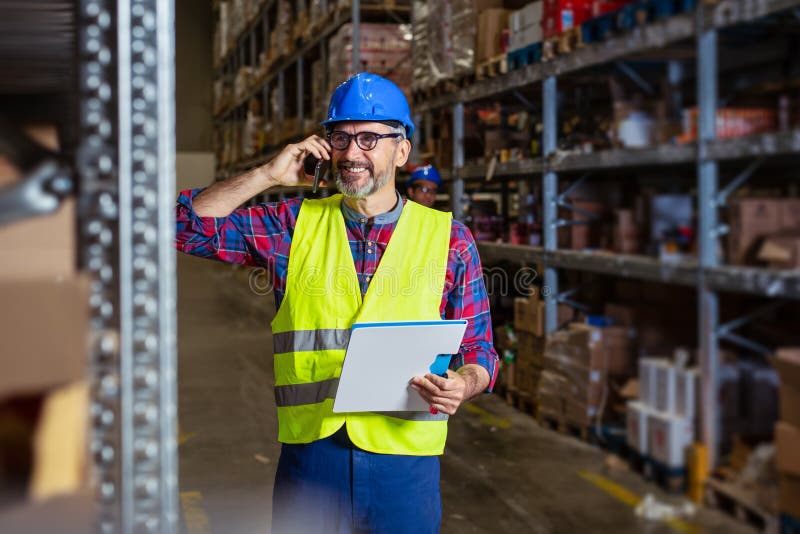 Warehouse worker talking on the phone holding clipboard in a large warehouse