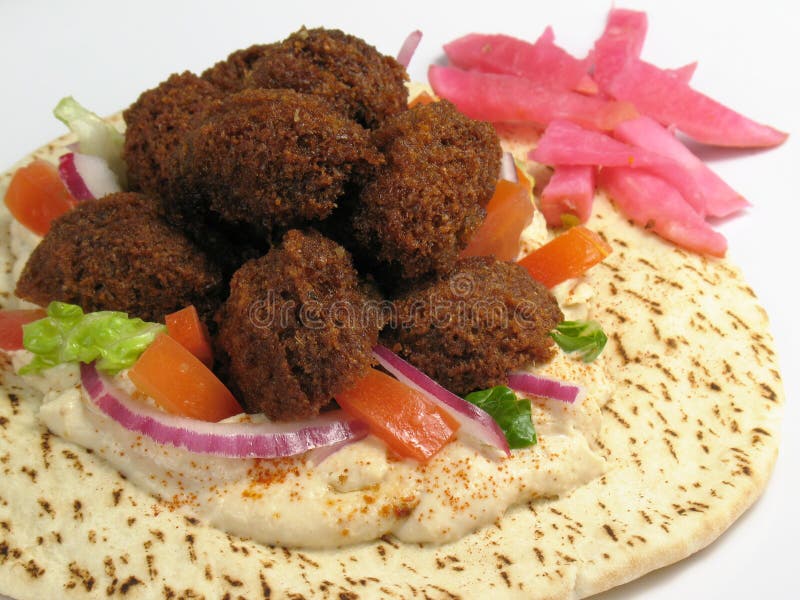 Una deliziosa porzione di falafels servita sulla cima di una pita con l'hummus, la lattuga, pomodoro, cipolla rossa, e un contorno di rape sottaceto nel barbabietole.