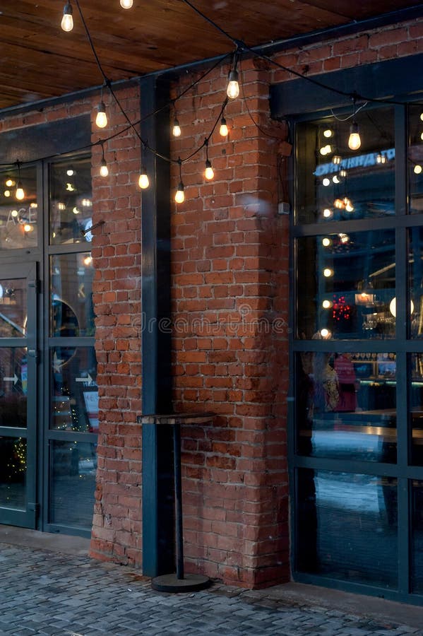 Warm industrial lights hang across a rustic brick facade creating a cozy evening mood. Industrial lights stock images, royalty-free photos and pictures