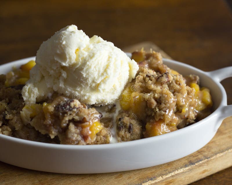 Warm peach cobbler with pecan streusel topping with a scoop of ice cream melting. Close up view. Warm peach cobbler with pecan streusel topping with a scoop of ice cream melting. Close up view.