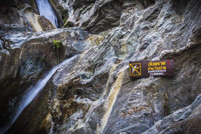 Warning Sign dangerous climbing at waterfall with stones.