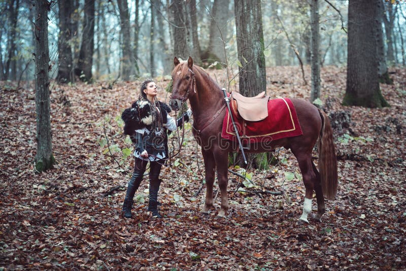 Warrior woman with her brown horse into the woods - Beautiful Scandinavian viking girl stock photos Warrior woman with her brown horse into the woods - Beautiful Scandinavian viking girl stock photos