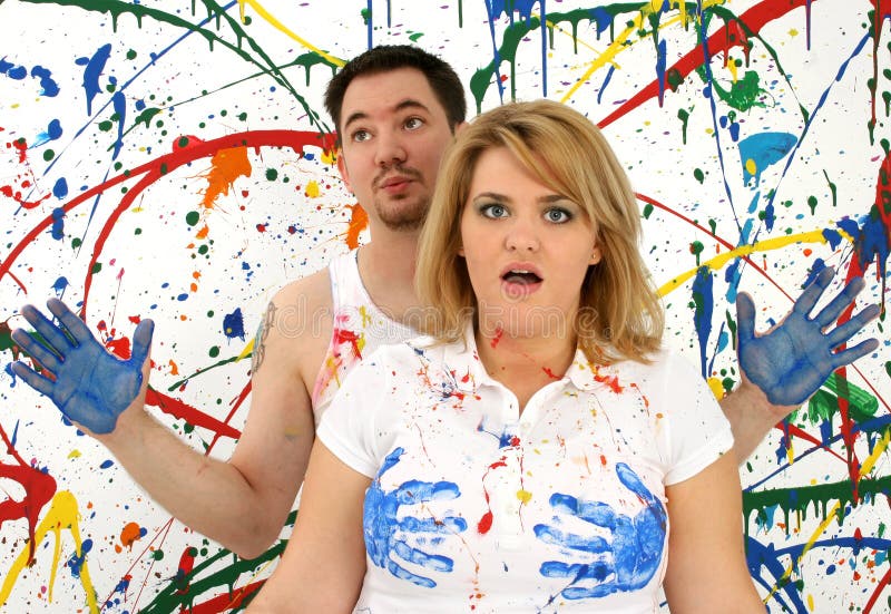 Young woman with shocked expression and blue hand prints on shirt with guilty looking man standing behind her. Young woman with shocked expression and blue hand prints on shirt with guilty looking man standing behind her.