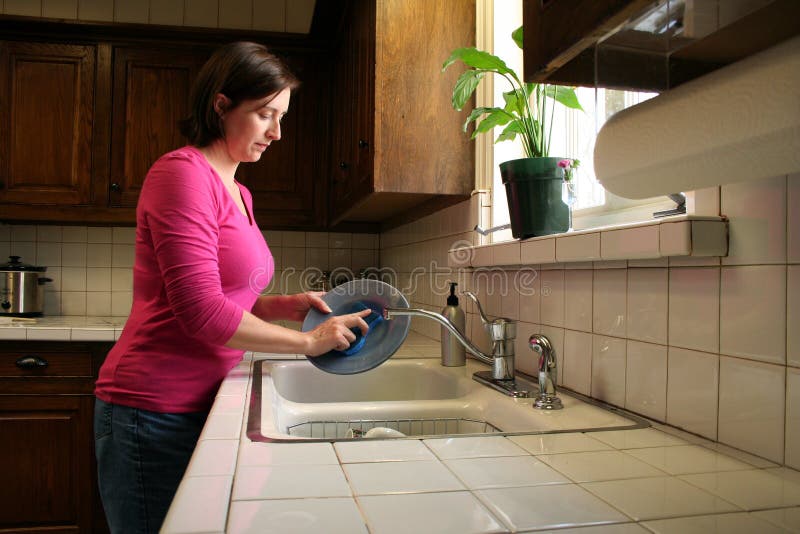 Una donna che lava i piatti al lavandino della cucina.