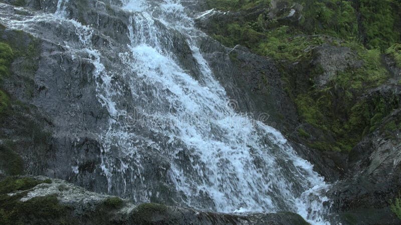 Wasser kaskadiert unten vertikale Steinleistenbrüche auf Stein und Schäume.