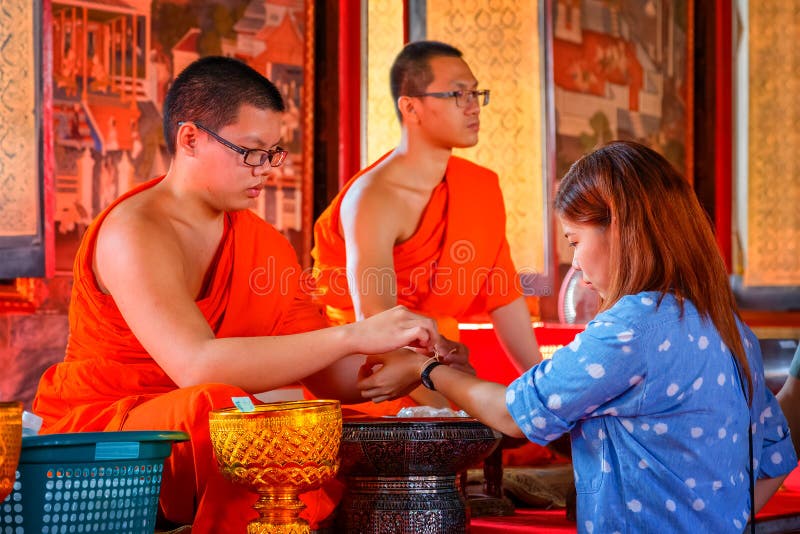 BANGKOK, THAILAND - JANUARY 2: Wat Arun in Bangkok, Thailand on January 2, 2015. Unidentified novice monk ties a ceremonial treat onto the wrist of a European tourist at Wat Arun - the Temple of Dawn. BANGKOK, THAILAND - JANUARY 2: Wat Arun in Bangkok, Thailand on January 2, 2015. Unidentified novice monk ties a ceremonial treat onto the wrist of a European tourist at Wat Arun - the Temple of Dawn