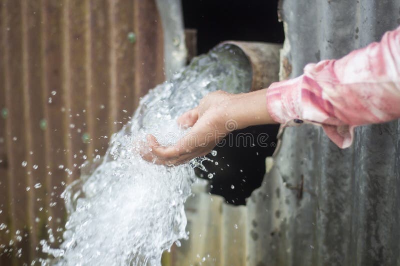 Water is Coming Out of a Pipe and a Boy is Catching the Water Stock