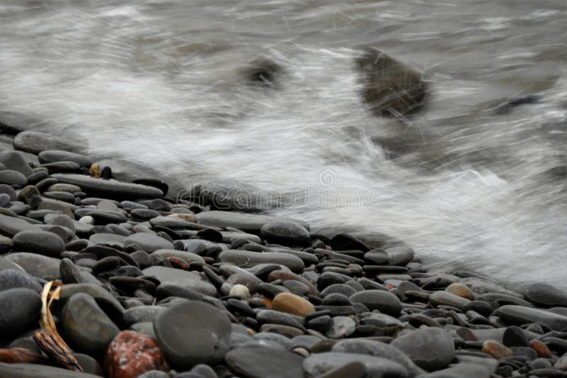 Onde di sovratensione sulla spiaggia di ciottoli e grigia, triste giorno.