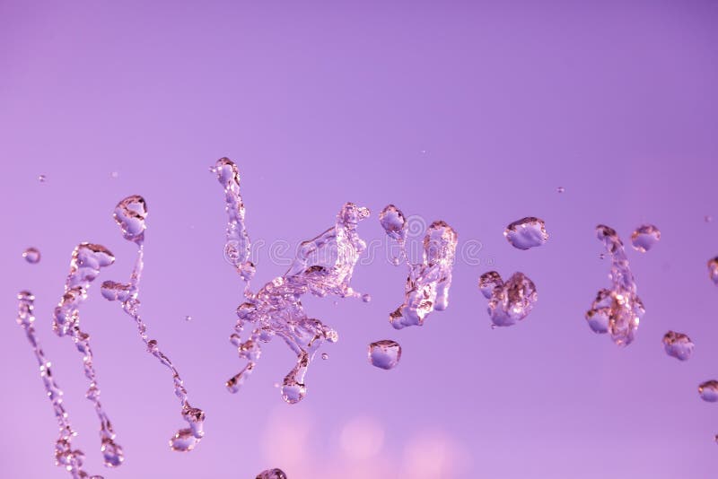 Water droplets frozen in the air with splashes and chain bubbles on a pink and purple isolated background in nature. Clear and stock photo Water droplets frozen in the air with splashes and chain bubbles on a pink and purple isolated background in nature. Clear and stock photo