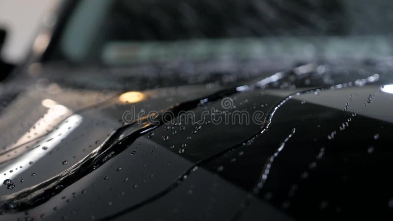 Water drops flow on a black vehicle after car wash