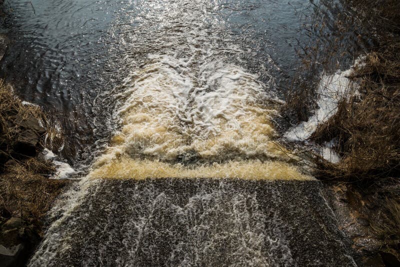 The water of the fast wild river falls from the concrete locks forming a waterfall and flows into the lake. water forms a white stock photo