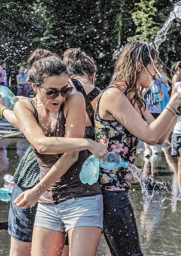 Water fight event in Bucharest. People having fun during the summer and cooling by throwing water from bottles. Wet clothes, wet hair, all wet, blur green background and water drops. 3 Young girls stay back in back trying to protect each other from the other participants. Water fight event in Bucharest. People having fun during the summer and cooling by throwing water from bottles. Wet clothes, wet hair, all wet, blur green background and water drops. 3 Young girls stay back in back trying to protect each other from the other participants.