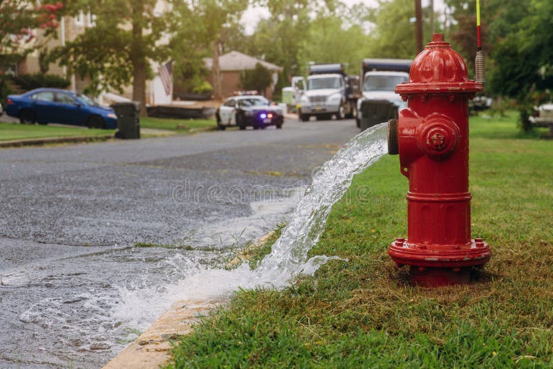 Water flowing from an open red fire hydrant is wet from the spray