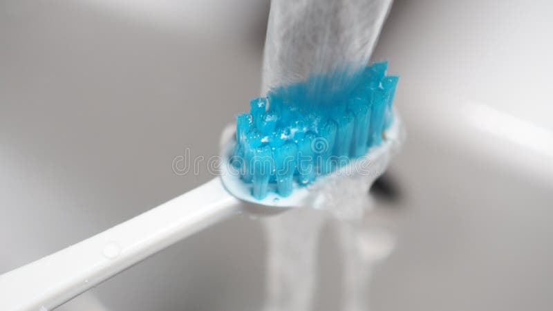 Water flows over a blue toothbrush in a bathroom sink stock image