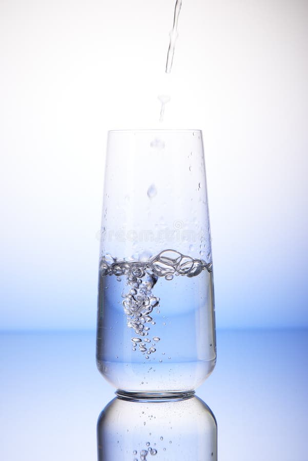 Water pouring into half-filled drinking glass with reflection on white and blue background. Water pouring into half-filled drinking glass with reflection on white and blue background