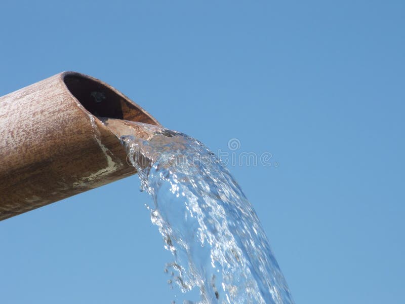 L'acqua che cade dal tubo Arrugginito contro il cielo blu.