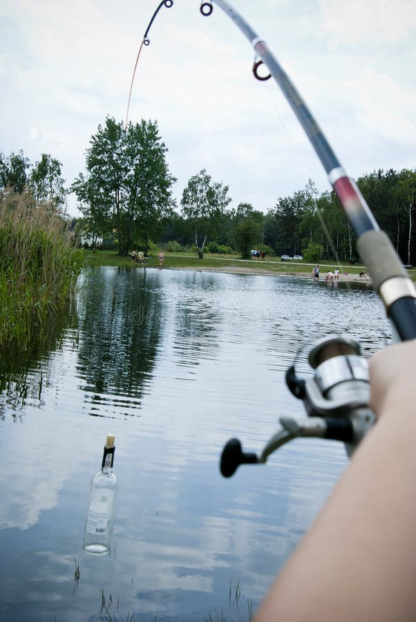 Mano che tiene una canna da pesca e la cattura di vuoto bottiglia di vino in stagno.