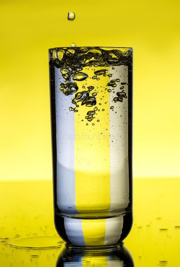 Water Pouring in Glass Over Yellow Background. Stock Photo Image of