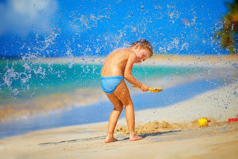 Water splashes on excited kid boy, on tropical beach