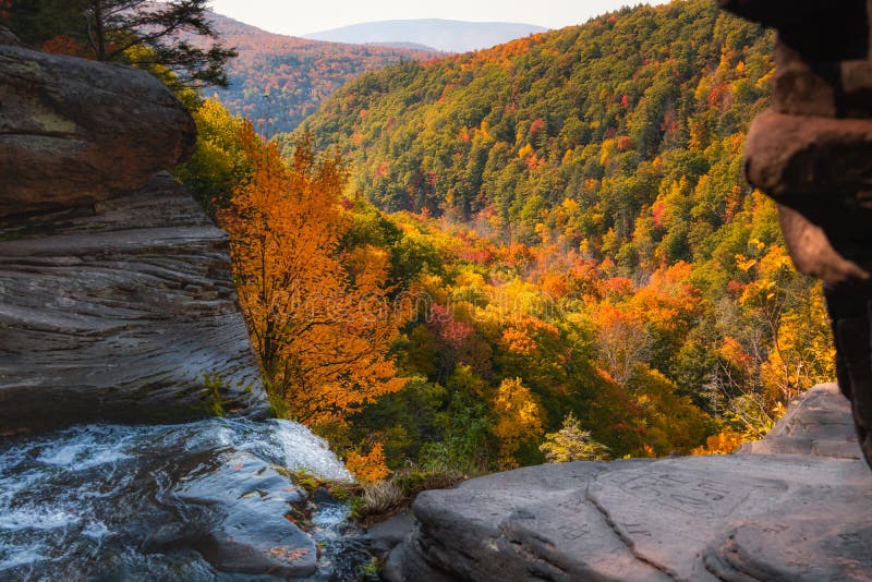 Water streaming off a rocky ledge leading into a valley valley fill with vibrant fall foliage color. Kaaterskill Falls - NY