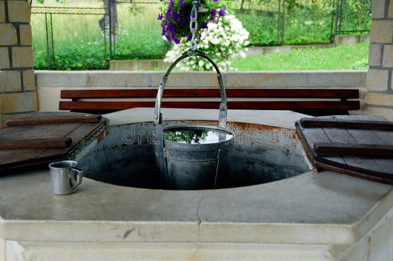 Bucket full of fresh water, water cup and an old water well.