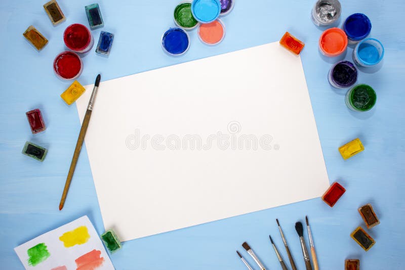 Watercolor, acrylic, brushes and a sheet of paper on a blue background. Flat lay, top view. artist`s table stock photo