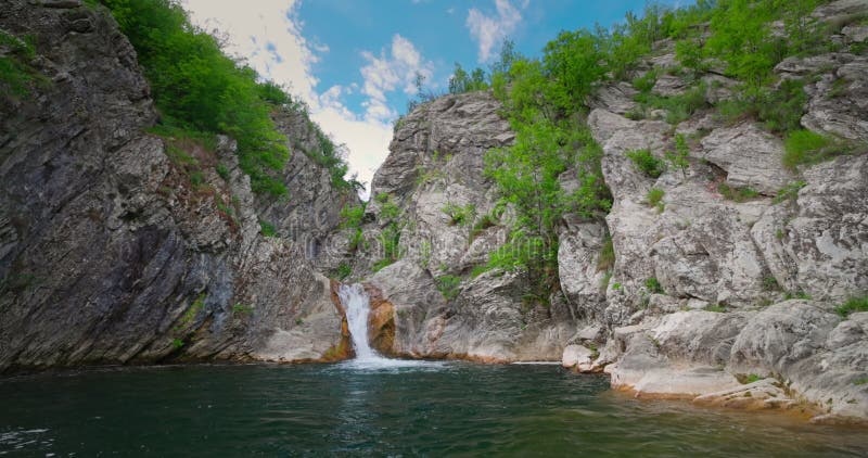 Waterfall in green forest and old stones. Blue pool and flowing stream.