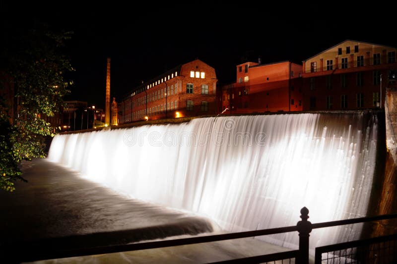 A picture taken at a waterfall in the dark. Location is in the industrial landscapes of Norrköping (Sweden). Brick houses in the background.