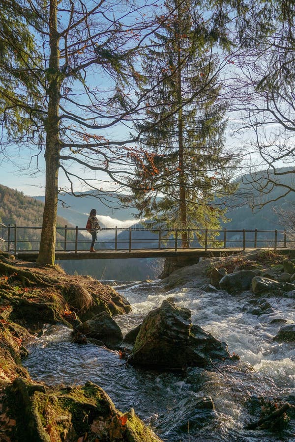 Waterfall scenery on top with bridge trees and hiking human woman view in the background fog landscape river with rocks and moss