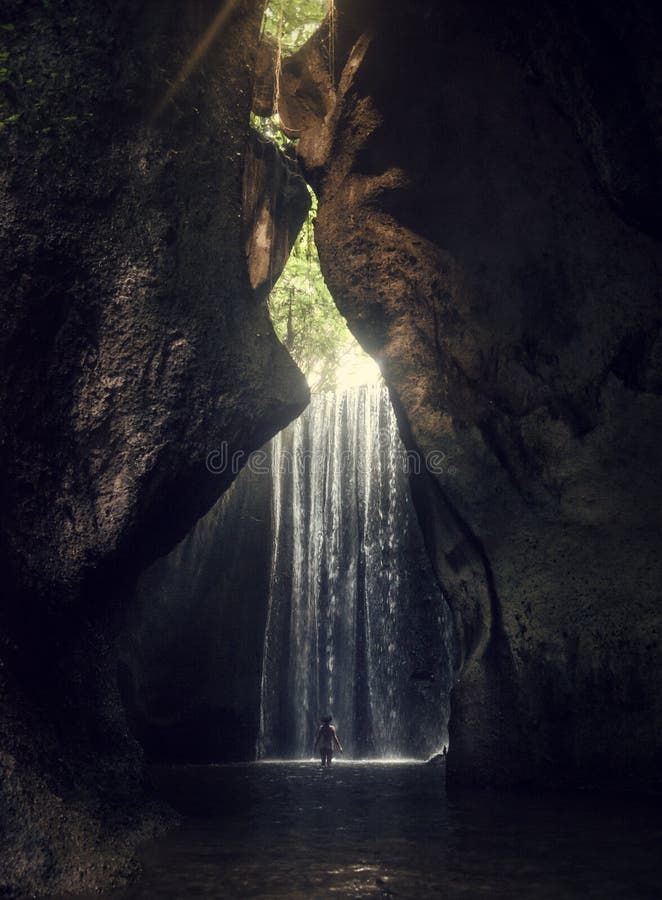 Waterfall Tukad Cepung. Waterfall in Bali. The gorge. A girl in a bathing suit at the waterfall.