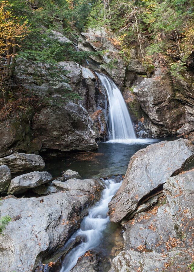 A waterfall and stream, framed by boulders, flows through colorful woods in autumn. A waterfall and stream, framed by boulders, flows through colorful woods in autumn