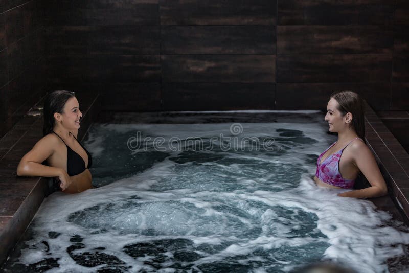 High angle side view of cheerful young girlfriends chilling together in bubbling water and enjoying hydro massage while spending time in spa pool. High angle side view of cheerful young girlfriends chilling together in bubbling water and enjoying hydro massage while spending time in spa pool