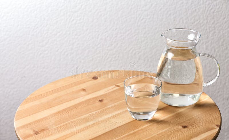 Waterkruik en glas met water op lijst dichtbij witte muur stock afbeelding Waterkruik en glas met water op lijst dichtbij witte muur stock afbeelding