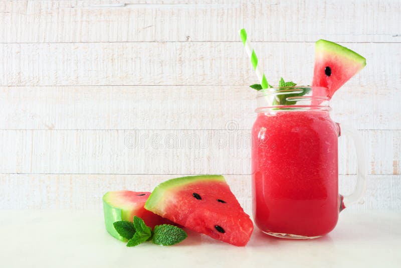 Watermelon juice in a mason jar with melon slices, side view against white wood
