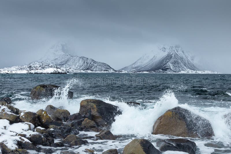 Waves crushing on the rocks on a beach from Lofoten Islands, Norway. Spectacular snowy mountains in the background. Moody winter stock photos Waves crushing on the rocks on a beach from Lofoten Islands, Norway. Spectacular snowy mountains in the background. Moody winter stock photos