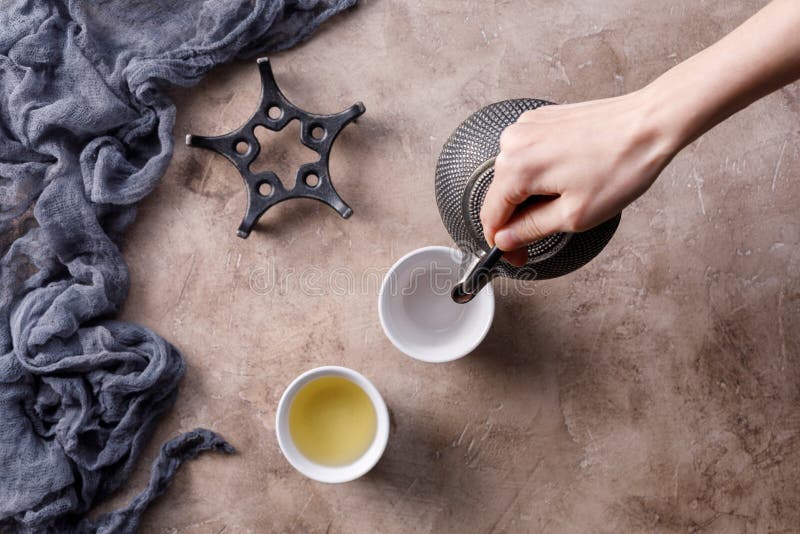 Wciąż życie z tradycyjną Azjatycką ziołową herbatą która nalewają od starego żeliwnego czajnika na textured tle z pialami, obraz stock Wciąż życie z tradycyjną Azjatycką ziołową herbatą która nalewają od starego żeliwnego czajnika na textured tle z pialami, obraz stock