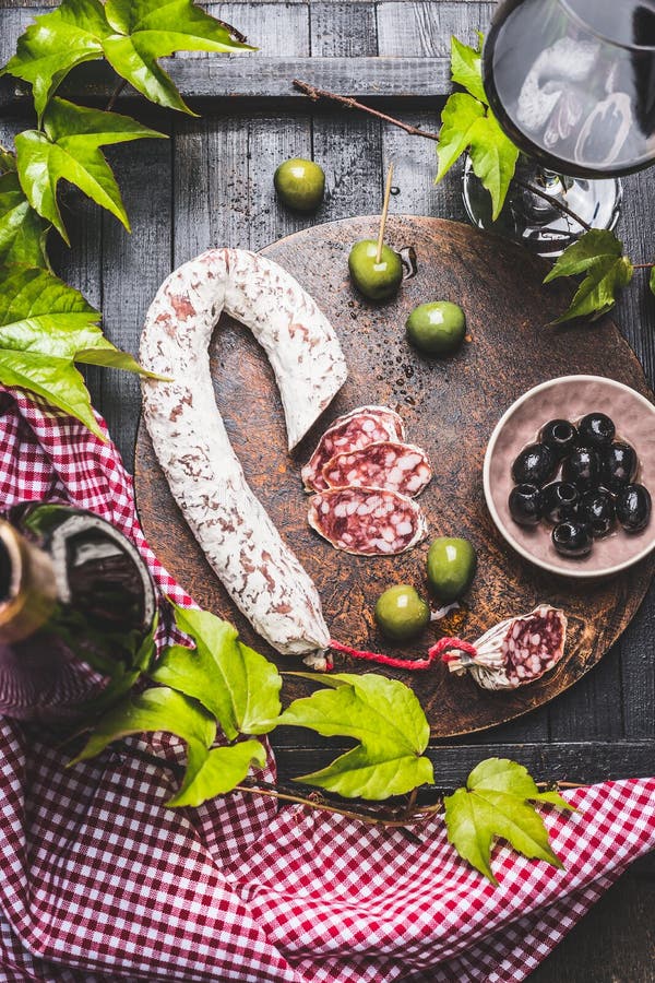 Still life with typical of Italian antipasti : salami,various olives, grape leaves and red wine on dark wooden kitchen table, top view. Italian food. Still life with typical of Italian antipasti : salami,various olives, grape leaves and red wine on dark wooden kitchen table, top view. Italian food