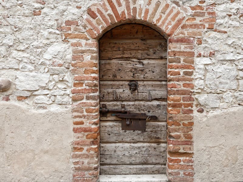Old brick masonry arch with weathered wooden door in thick stone wall
